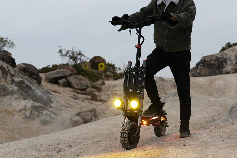 Trottinette électrique phares allumés au crépuscule sur un sentier rocheux