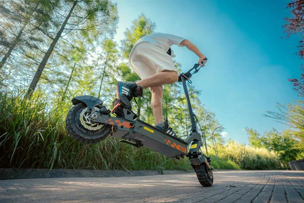 Conducteur sautant d’un trottoir avec une trottinette KuKirin noire et orange – KuKirin G2 Pro vs G4 vs G2 Master