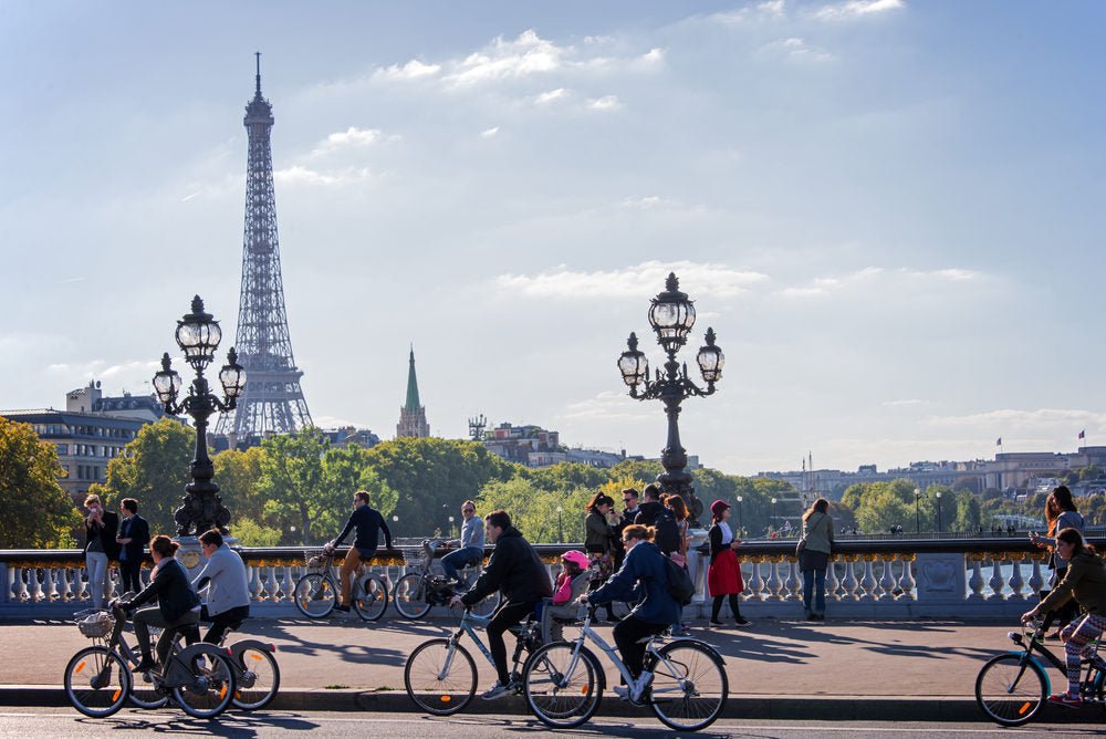 Cyclistes sur un pont à Paris, tour Eiffel au fond, dont un enfant casqué sur un siège vélo – réglementation vélo électrique