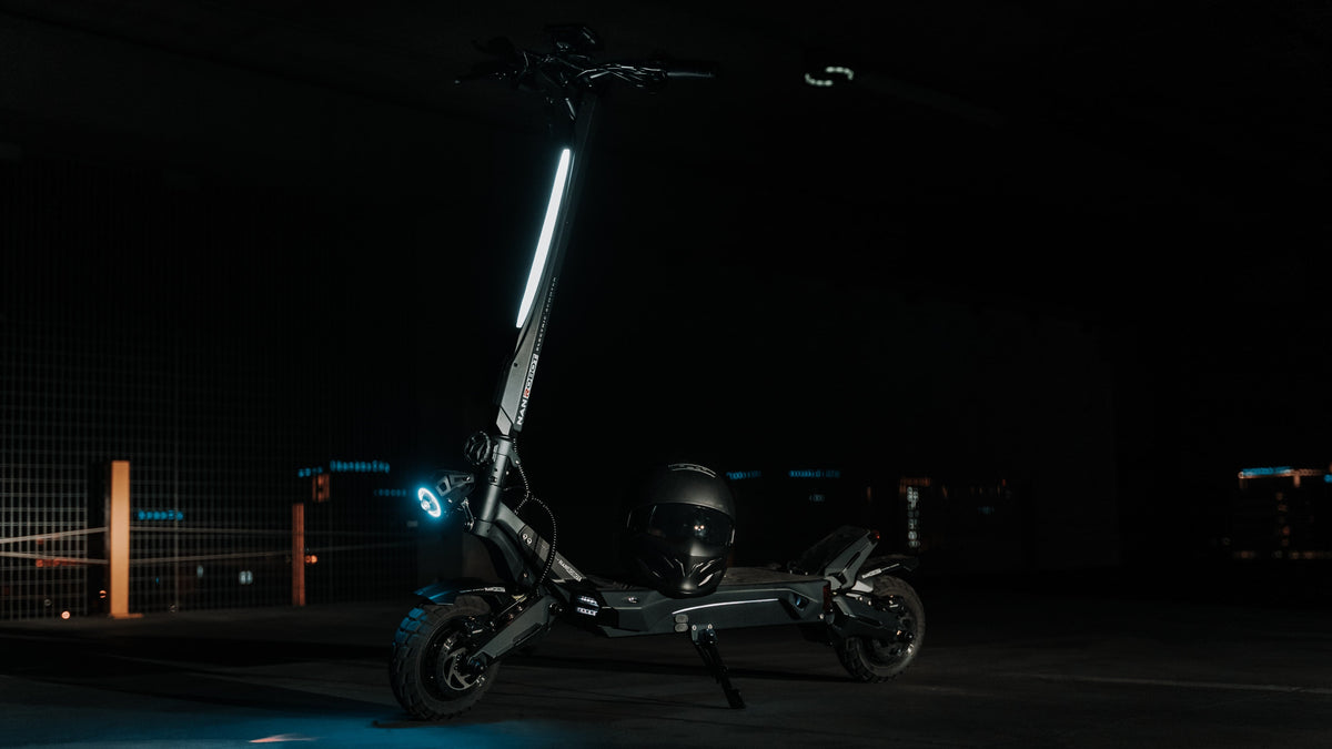 Trottinette électrique noire garée sur sa béquille dans un garage sombre, un casque posé sur le plateau