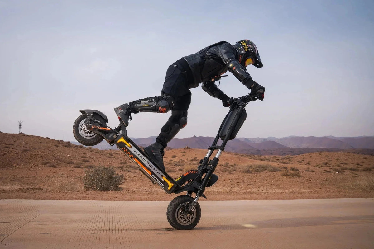 Pilote casqué, roue arrière levée, sur une trottinette électrique KuKirin noire et orange, route dans le désert