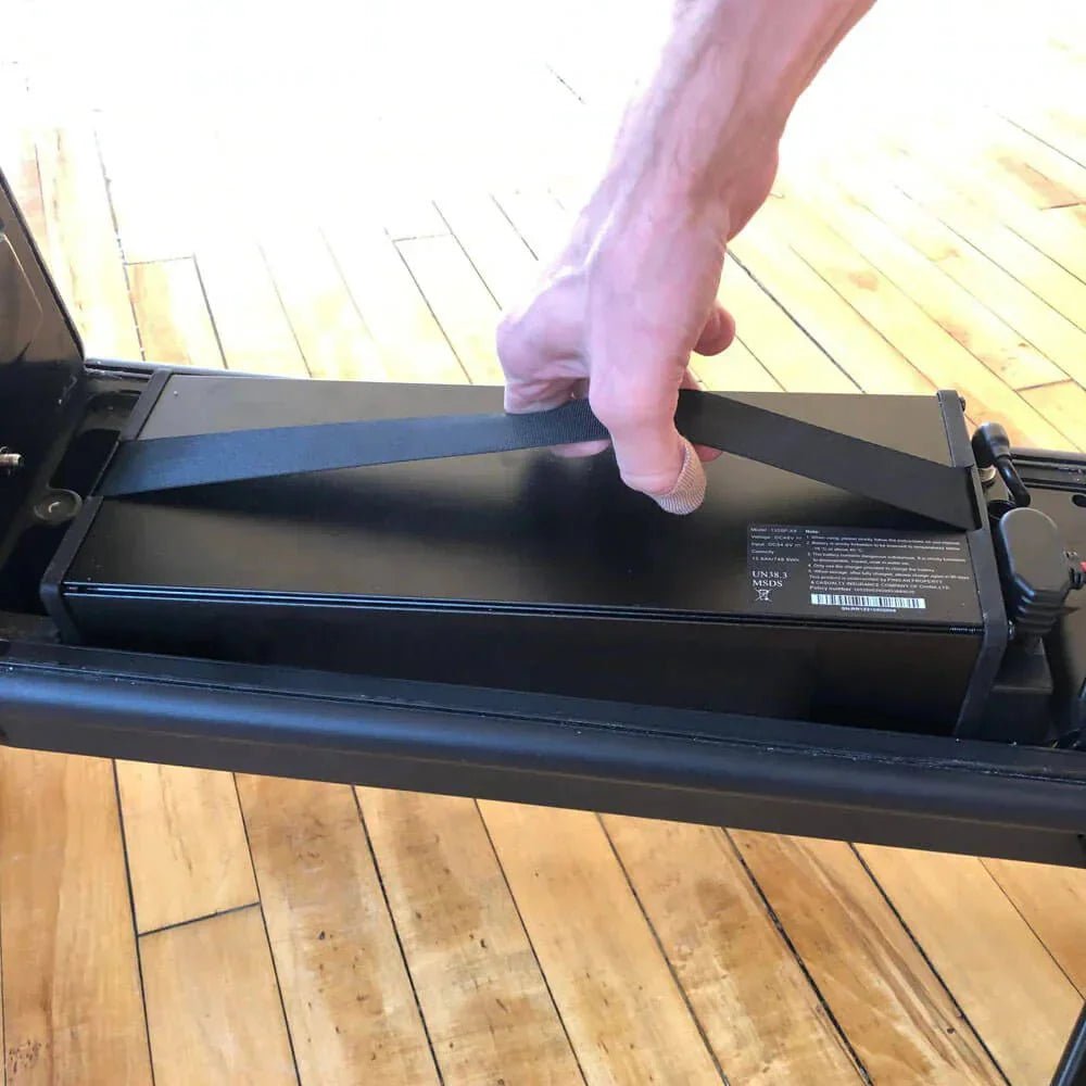 Main qui retire par sa sangle la batterie amovible d'une trottinette électrique, à l'intérieur, où elle se recharge le mieux