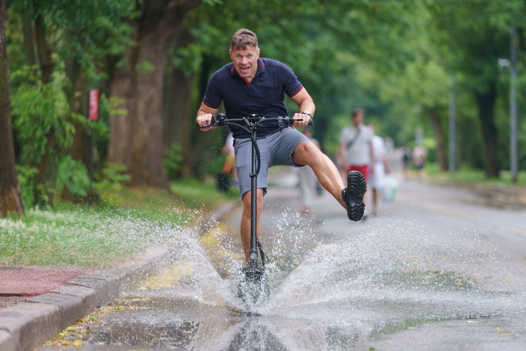 Un homme traverse une grande flaque en trottinette électrique et l’eau gicle – rouler sous la pluie et indice IP