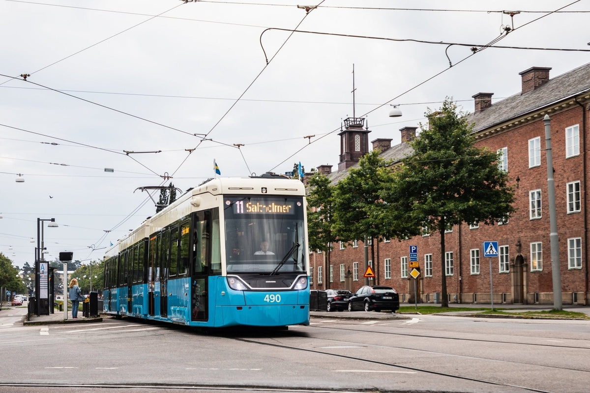 Tramway bleu et blanc de la ligne 11 vers Saltholmen dans une rue de Göteborg, près d’un arrêt et d’un bâtiment en brique