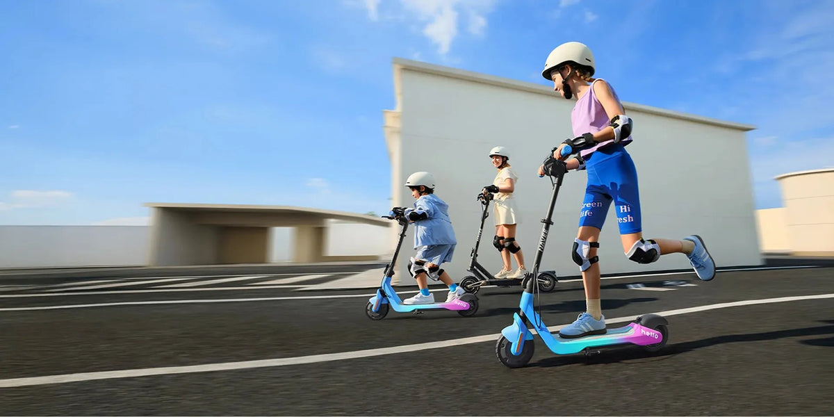 Trois enfants avec casque, genouillères et coudières roulent en trottinette électrique sur une place goudronnée ensoleillée