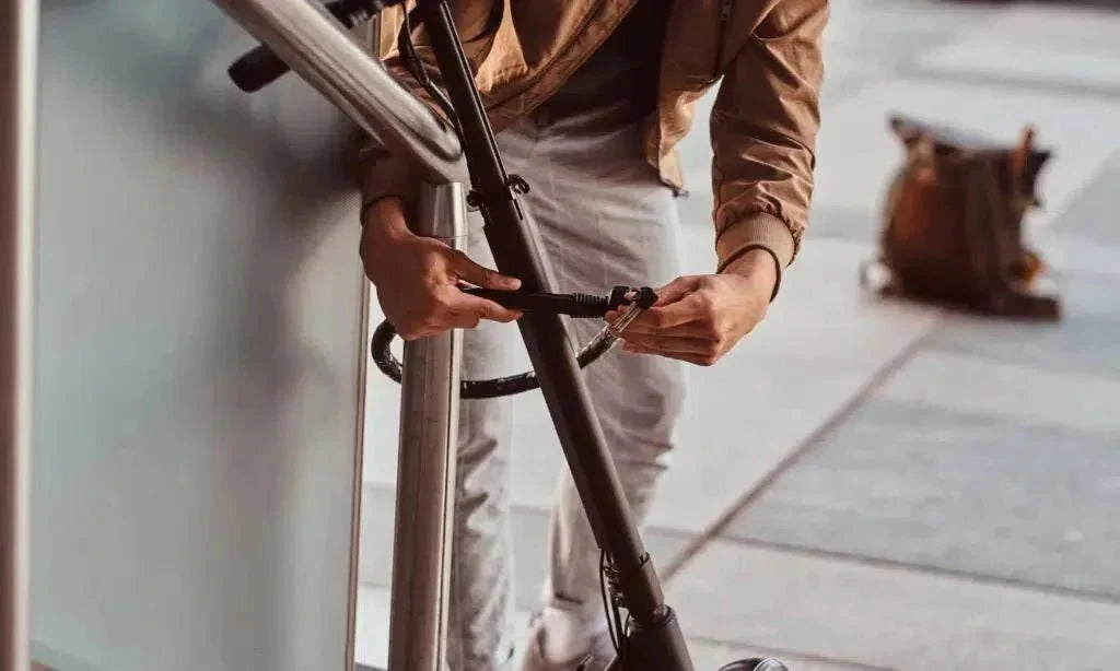 Une personne attache une trottinette électrique à une rampe avec un câble antivol fin – protéger sa trottinette du vol
