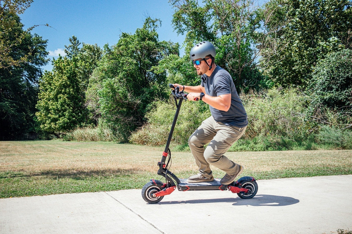 Homme casqué à lunettes de soleil sur une trottinette électrique robuste à suspensions, sur une allée bétonnée d’un parc