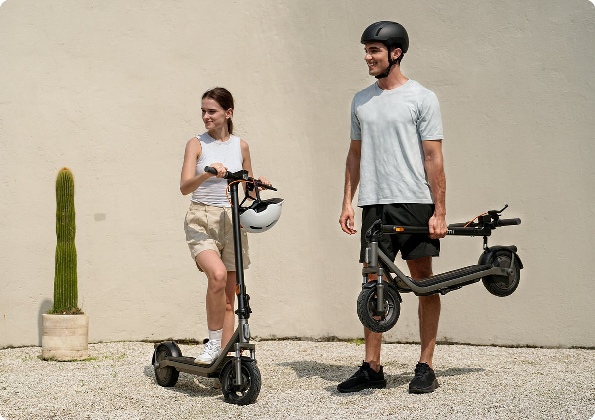 Deux personnes avec chacune une trottinette électrique Xiaomi devant un mur clair et un cactus, l’homme porte un casque