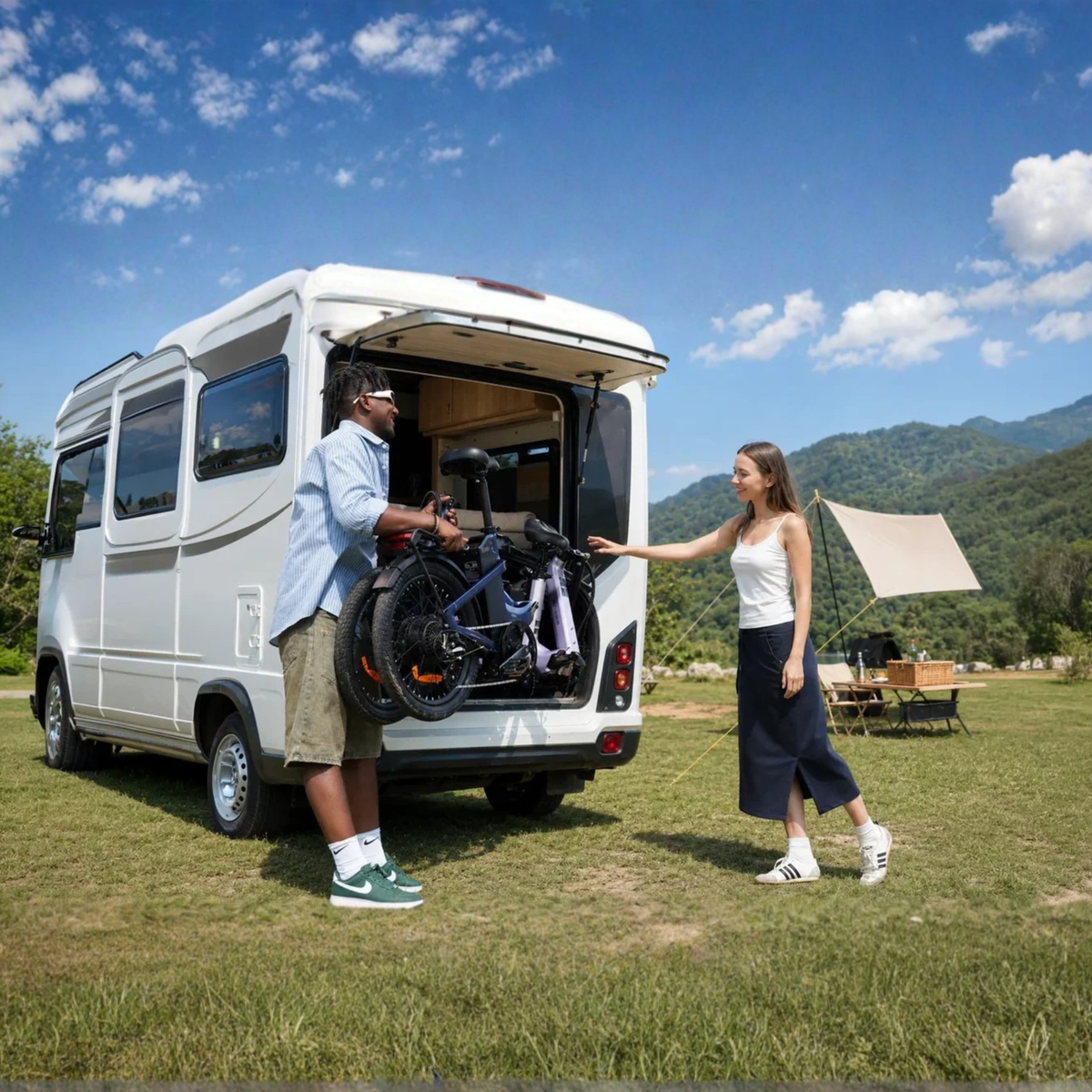ENGWE O20 Boost – homme soulevant un vélo plié dans un camping-car blanc pendant qu’une femme se tient à côté, prairie et montagnes en arrière-plan