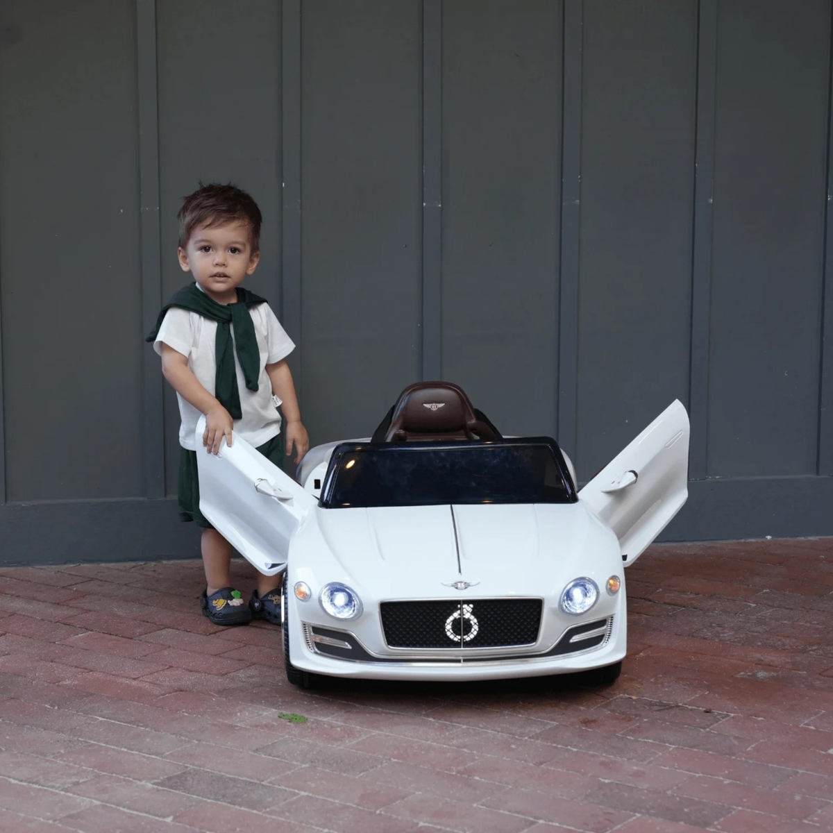 Enfant au volant de la voiture électrique pour enfants Bentley EXP 12 avec un adulte à côté