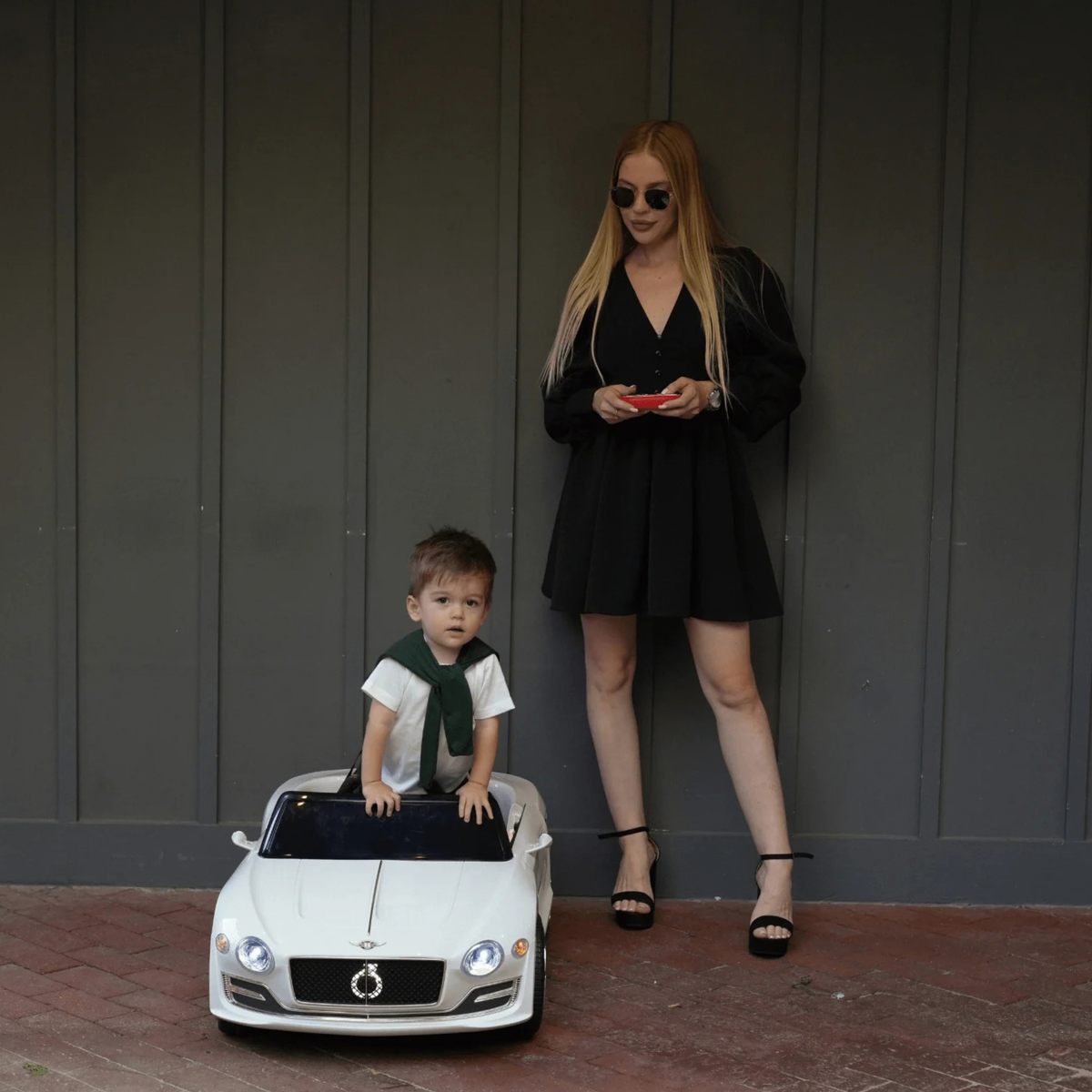 Enfant au volant de la voiture électrique pour enfants Bentley EXP 12 avec un adulte à côté