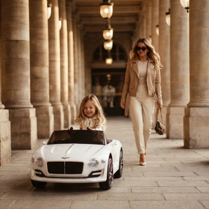 Enfant au volant de la voiture électrique pour enfants Bentley EXP 12 avec un adulte à côté