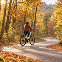 Femme casquée à vélo sur un OneSport OT12 Pro blanc sur un chemin forestier parmi les feuilles d'automne
