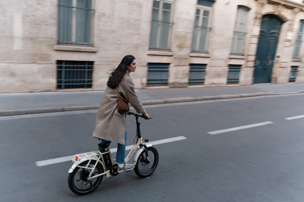 OneSport OT16 Pro : femme en manteau à vélo dans une rue devant une façade en pierre, vue de côté