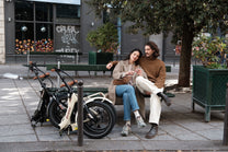 Un couple assis sur un banc à côté de deux vélos pliés OneSport, l'un beige et l'autre noir
