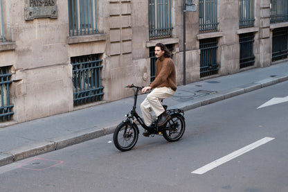 Homme à vélo sur l'OneSport OT16 Pro, vélo noir, dans une rue le long d'un bâtiment en pierre avec des fenêtres à barreaux