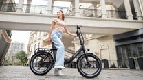 OneSport OT16 Pro : vélo noir vu de côté avec une femme debout à côté sur une place pavée