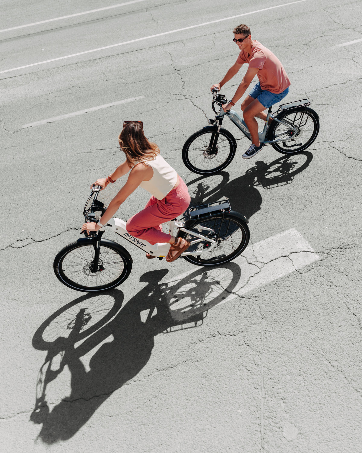 OneSport WT05 vu du dessus, une femme sur un vélo blanc et un homme sur un vélo gris roulent sur l'asphalte avec des ombres