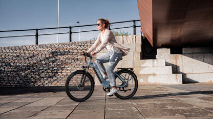 Femme à vélo sur un OneSport WT05 vu de profil devant un escalier en pierre et un mur en brique