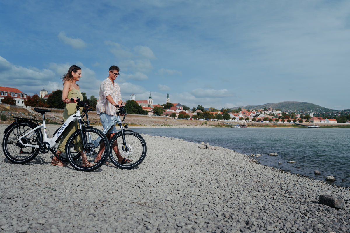Deux personnes poussant chacune un OneSport WT05 le long d'une plage de galets avec la ville et une colline à l'arrière-plan