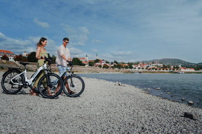 Deux personnes poussant chacune un OneSport WT05 le long d'une plage de galets avec la ville et une colline à l'arrière-plan