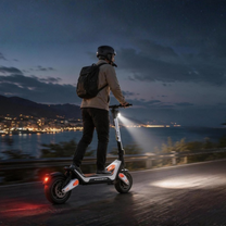 Personne avec casque et sac à dos roulant en Wheely - J18 sur une route côtière au crépuscule, phare allumé