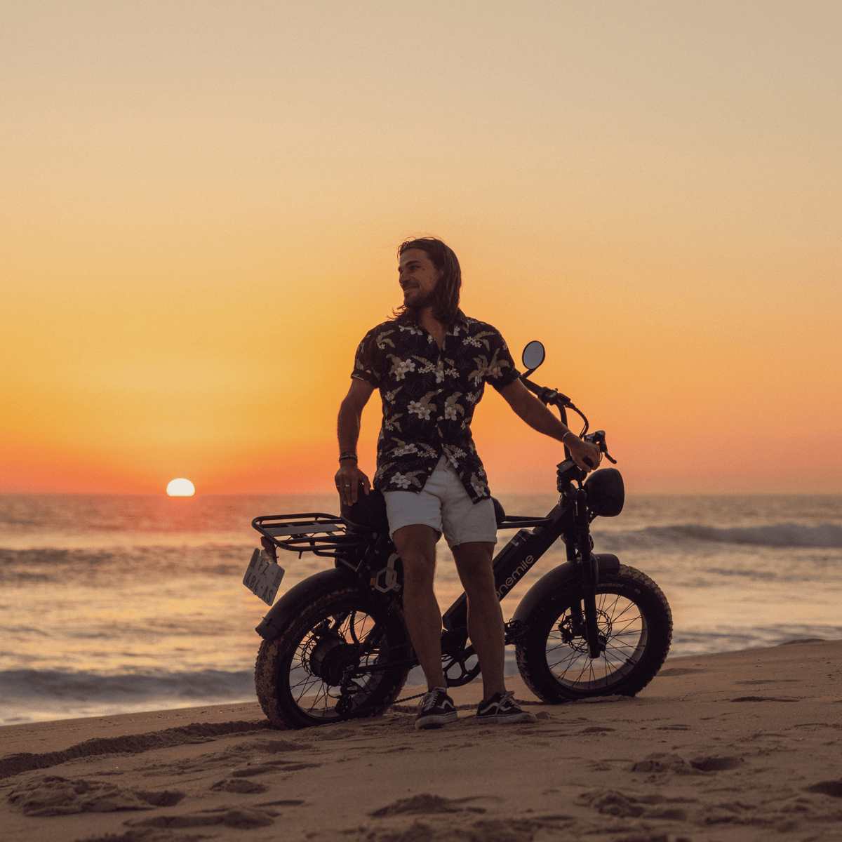 Homme debout avec le vélo électrique fat bike Onemile P40 Pro au bord de la mer au coucher du soleil