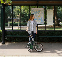 Femme debout avec le vélo électrique pliant OneSport OT02 en ville