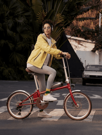 Femme roulant sur le vélo électrique pliant OneSport OT02 Pro coloris rouge dans une rue