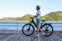 Femme debout avec le vélo électrique OneSport OT12 coloris noir au bord de la mer
