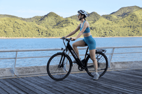 Femme assise sur le vélo électrique OneSport OT12 coloris noir au bord de la mer