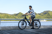 Homme assis sur le vélo électrique OneSport OT12 coloris noir au bord de la mer