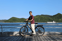 Homme debout avec le vélo électrique OneSport OT12 coloris noir au bord de la mer