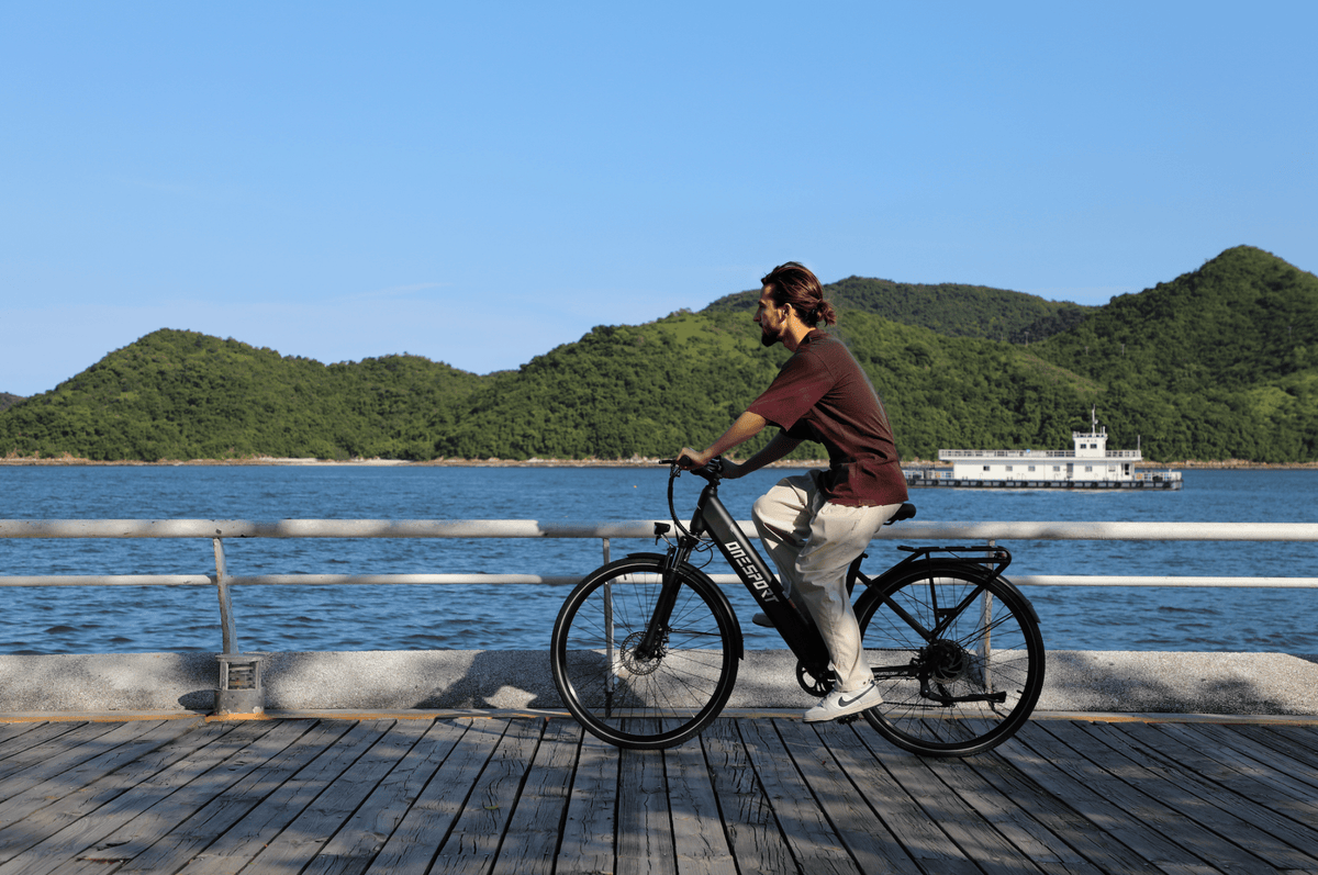 Homme roulant sur le vélo électrique OneSport OT12 coloris noir au bord de la mer