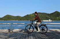 Homme roulant sur le vélo électrique OneSport OT12 coloris noir au bord de la mer