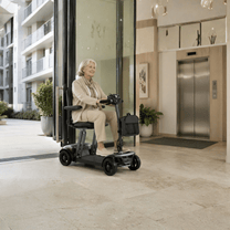 Femme âgée assise sur le scooter de mobilité Sweetrich Air Traveller en intérieur