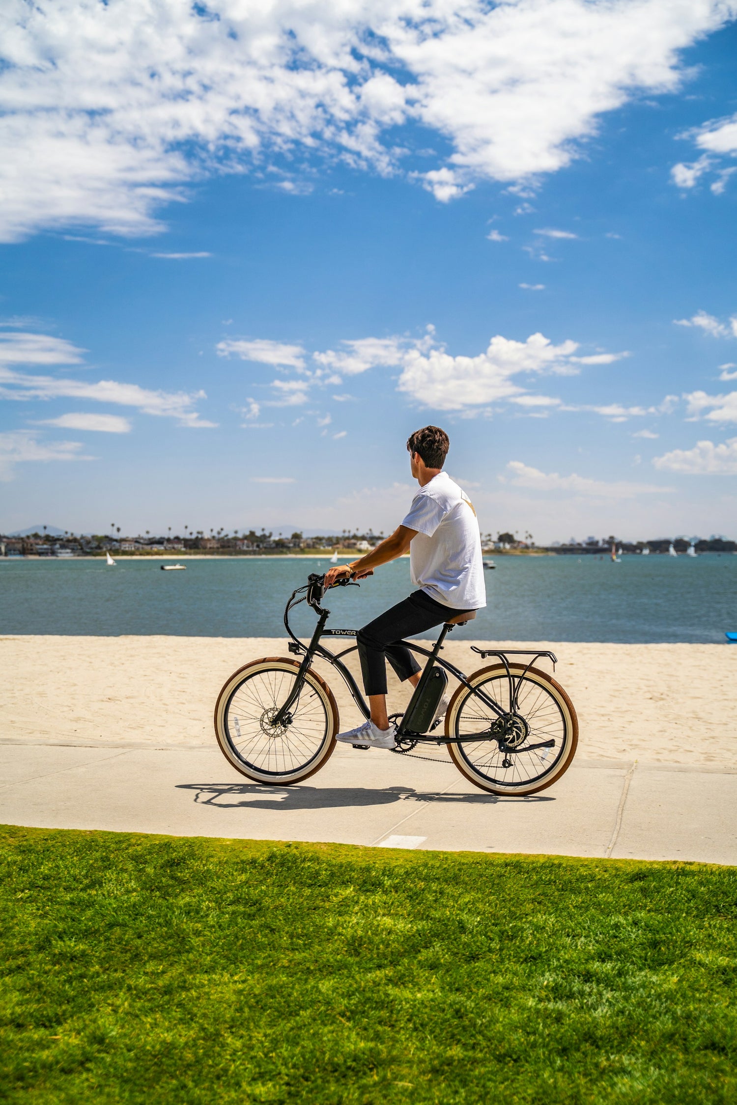 En man som kör på en elcykel på trottoaren längs en strandpromenad med havet i bakgrunden