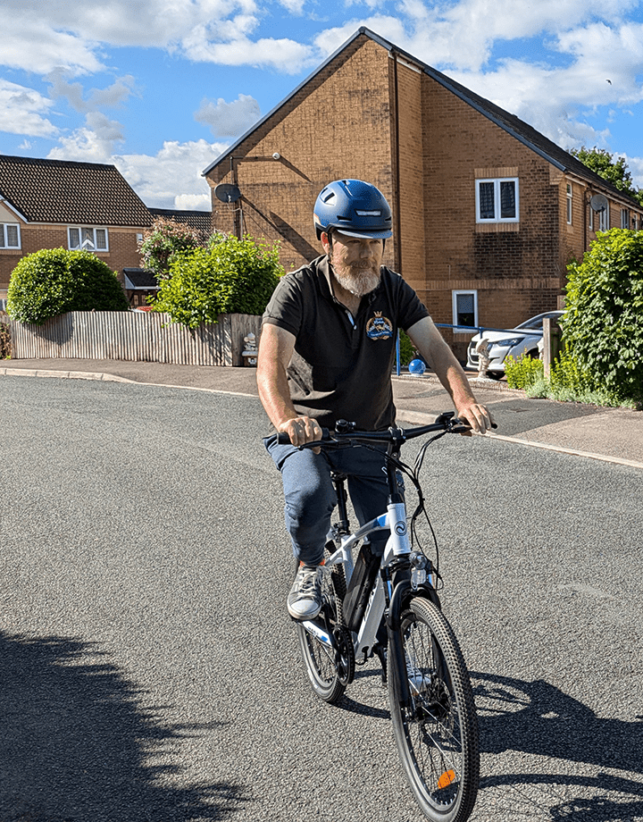 Homme roulant sur le VTT électrique VARUN M24-1 coloris blanc avec un casque dans une rue