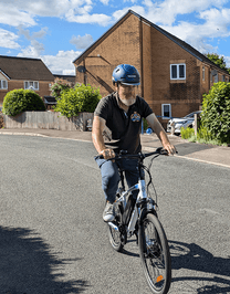 Homme roulant sur le VTT électrique VARUN M24-1 coloris blanc avec un casque dans une rue