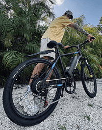 Homme roulant sur le VTT électrique VARUN M24-1 coloris noir sur un chemin de gravier