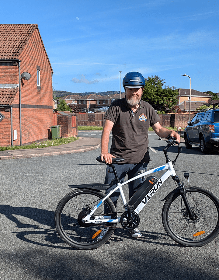 Homme debout avec le VTT électrique VARUN M24-1 coloris blanc avec un casque dans une rue