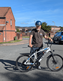 Homme debout avec le VTT électrique VARUN M24-1 coloris blanc avec un casque dans une rue